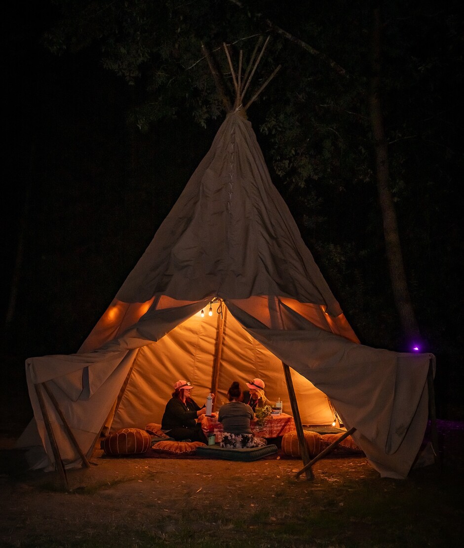 Attendees relaxing inside a lit teepee at night at Camp Navarro